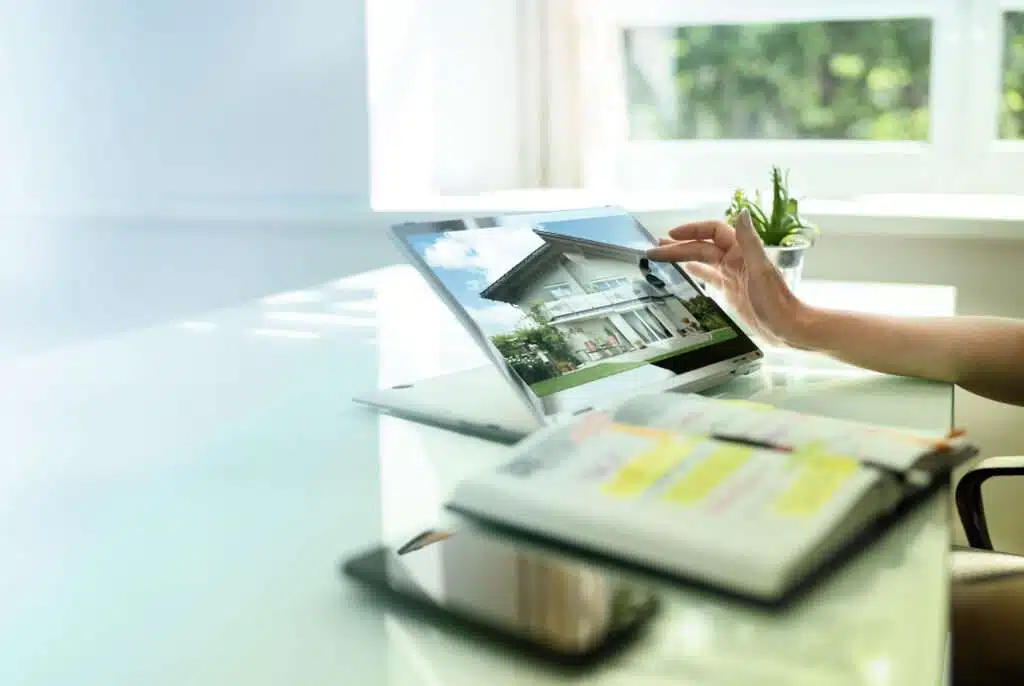 Eine Person sitzt am Tisch mit einem Handy und Tablet, auf dem ein neues Haus zu sehen ist, was auf ein Beratungsgespräch zu Fördermitteln hinweist